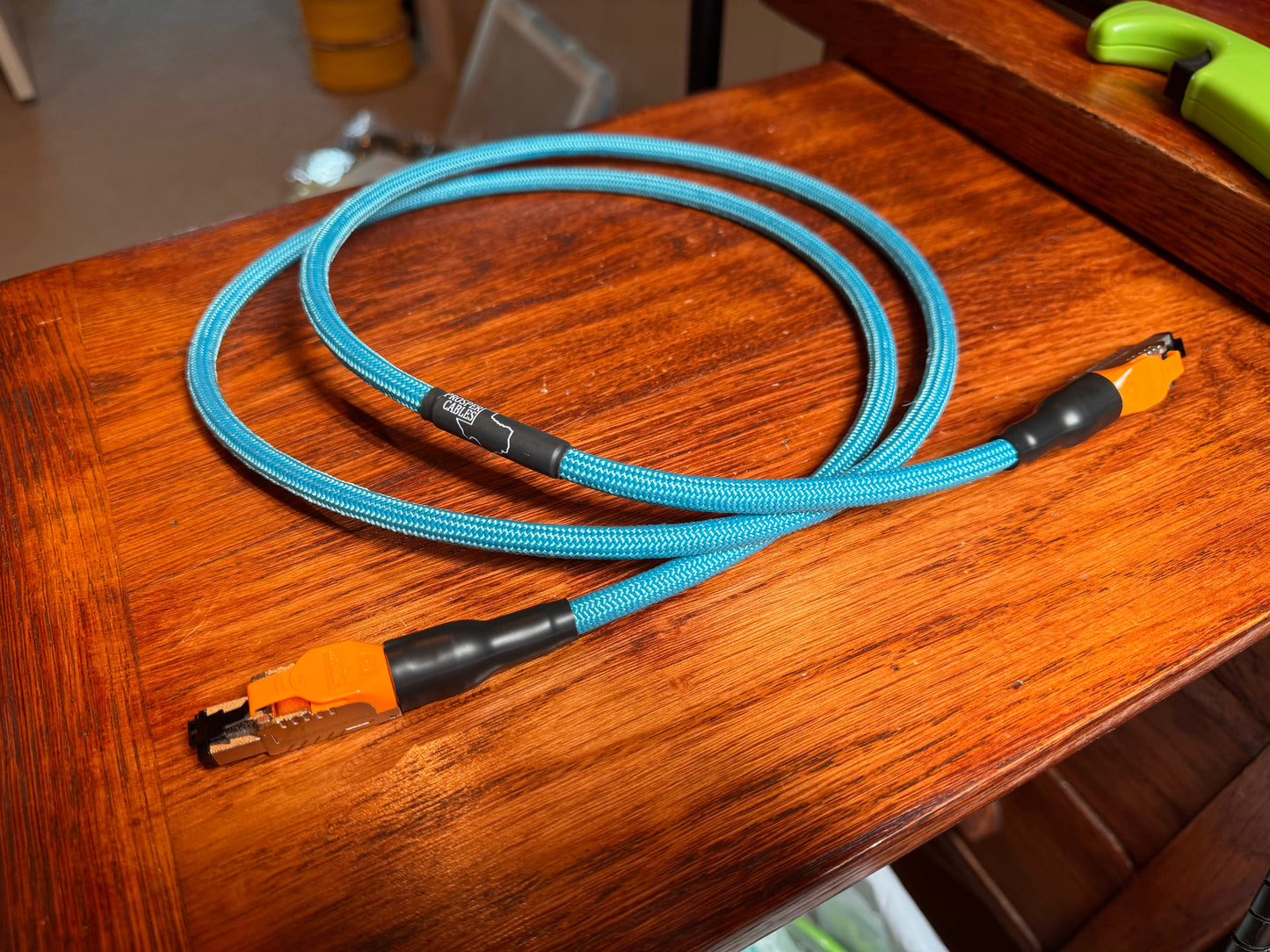 A blue and orange cable is lying on a wooden surface, with a green object visible in the background.