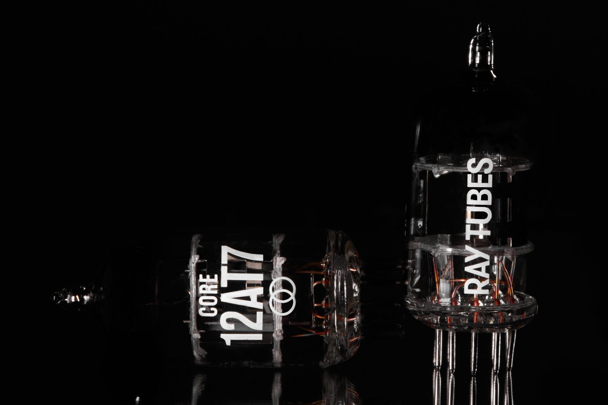 Two glass Ray Tubes, one labeled 'CORE 12AT7' and the other 'RAY TUBES', displayed on a reflective black surface against a solid black background.