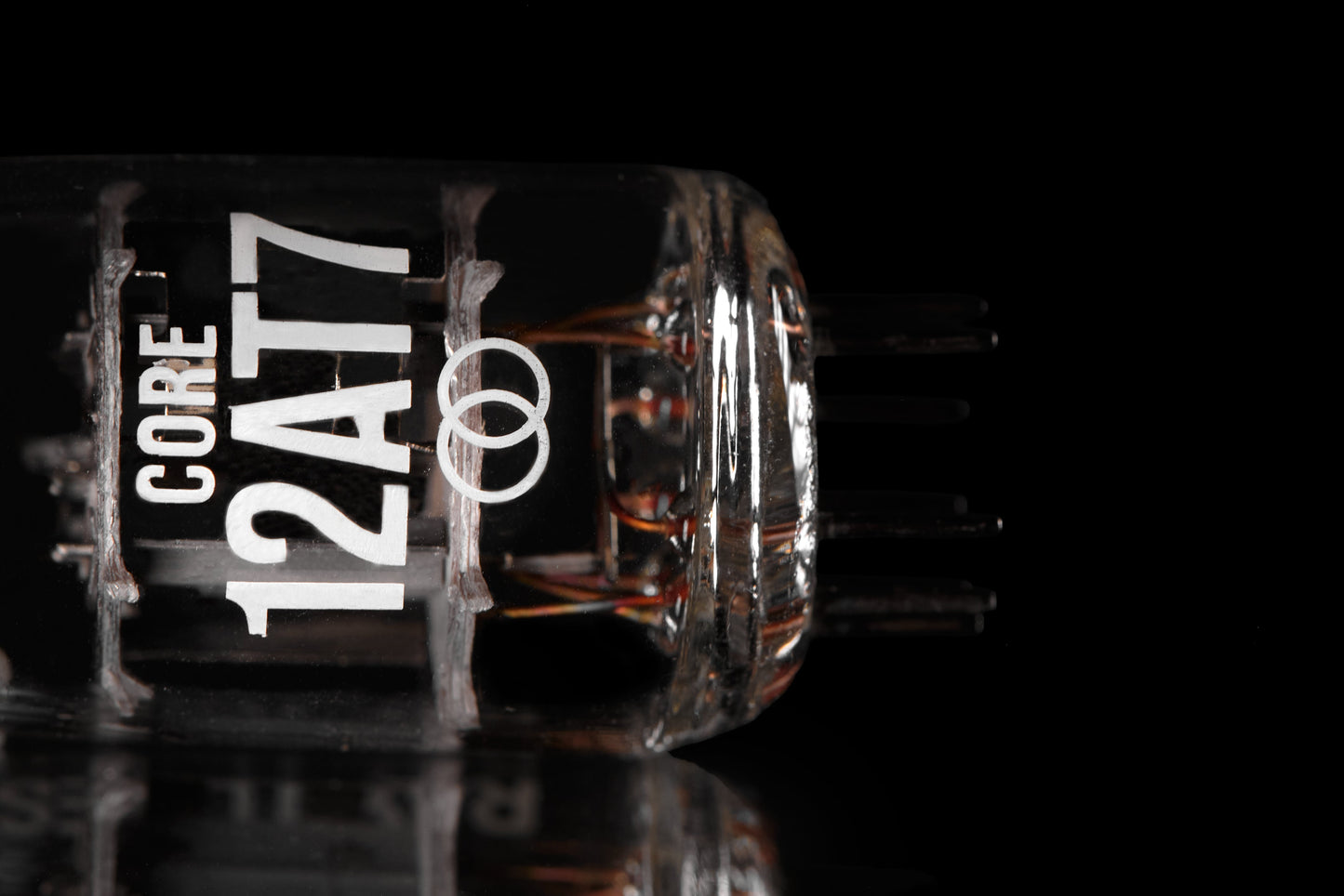 A close-up studio shot of a clear glass vacuum tube labeled 'CORE 12AT7' in white text, with internal copper filaments visible, set against a black background with a reflective surface below.