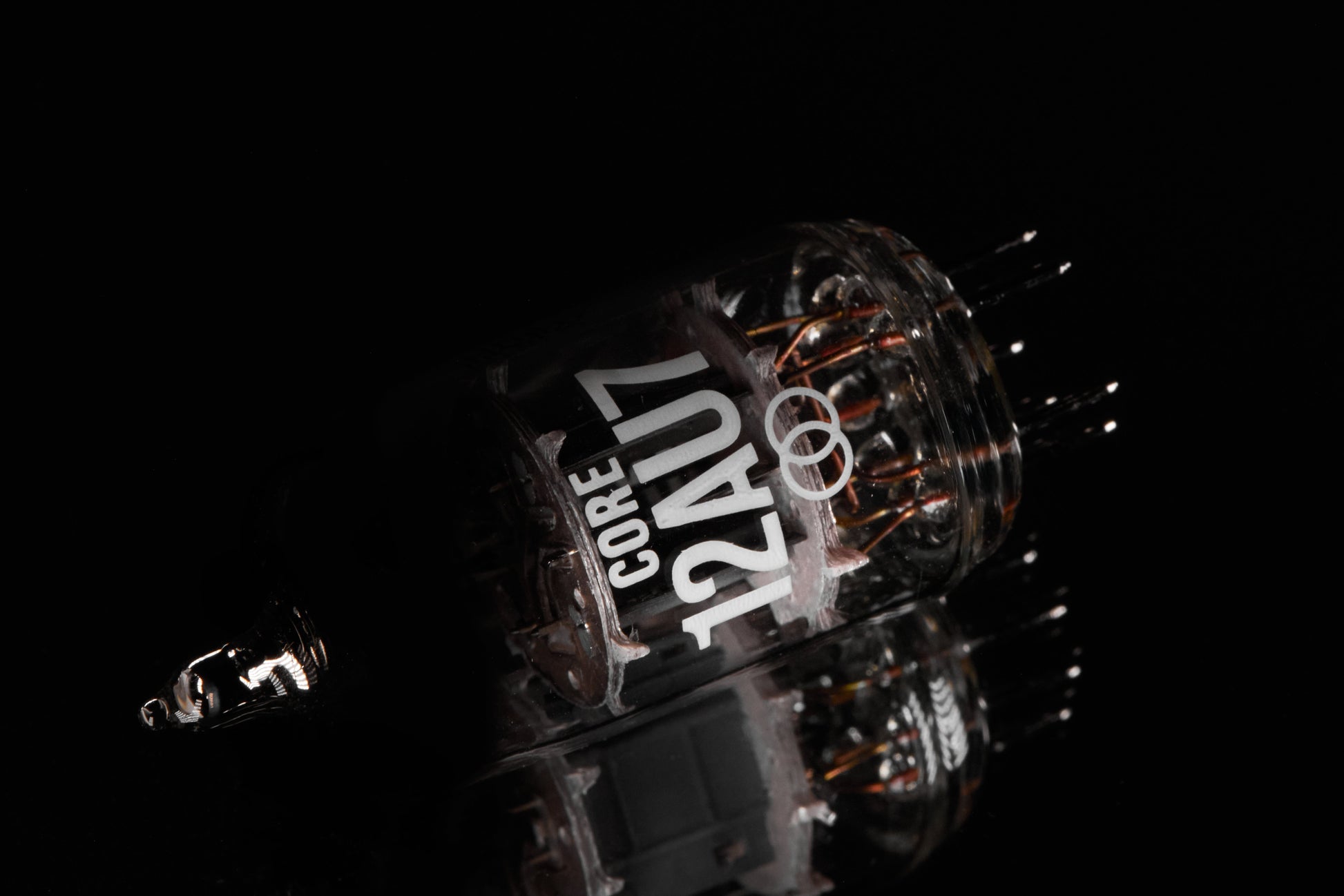 A close-up studio shot of a transparent glass vacuum tube labeled 'CORE 12AU7' with copper-colored internal filaments, photographed on a black reflective surface.