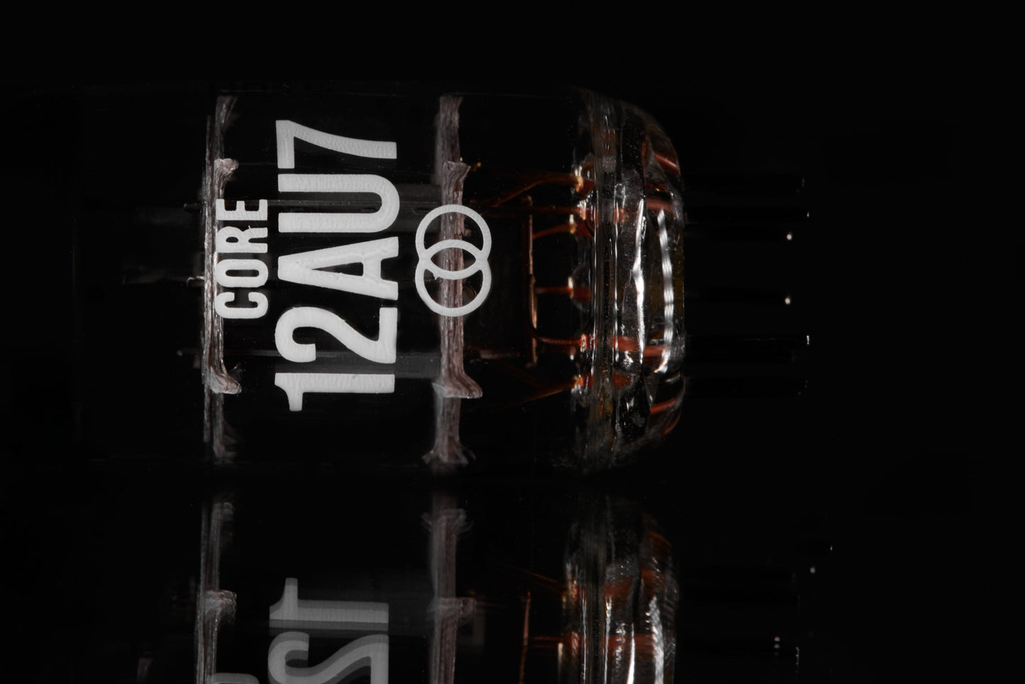 A close-up of a Core 12AU7 vacuum tube on a reflective black surface, showing its glass body, internal filaments, and printed white text.