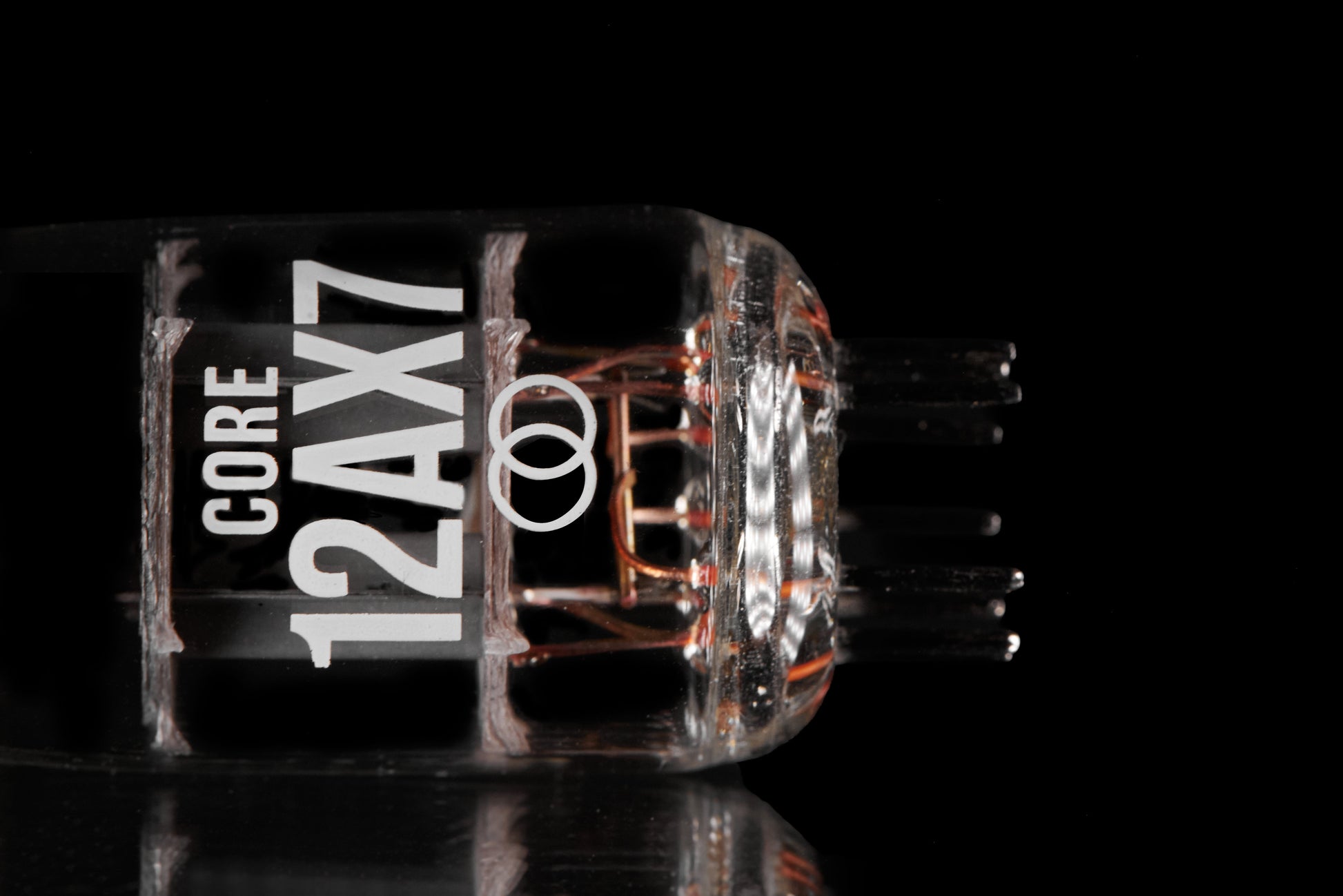 A close-up studio shot of a transparent glass vacuum tube labeled 'CORE 12AX7' with copper-colored internal filaments, set against a solid black background with a subtle reflection below.