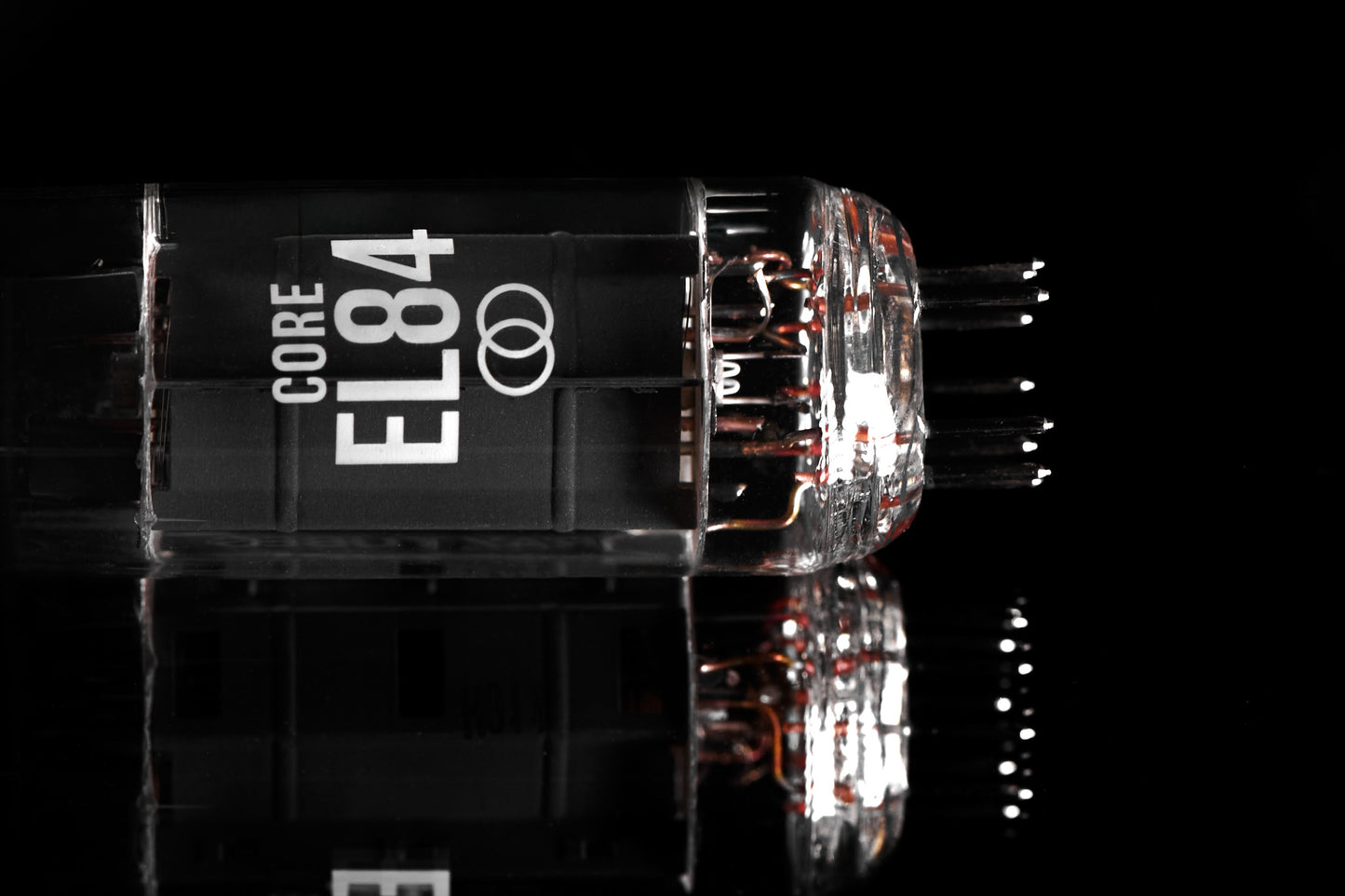 A close-up studio shot of a glass vacuum tube labeled 'CORE EL84' on a glossy black reflective surface.