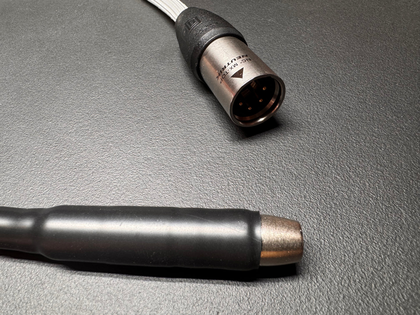 Close-up of a black and silver audio cable connector on a textured dark gray surface.