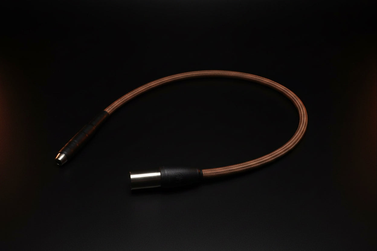 A brown braided audio cable with black and silver metal connectors, laid out on a gridded cutting mat.