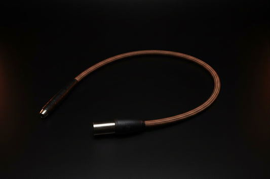 A brown braided audio cable with black and silver metal connectors, laid out on a gridded cutting mat.