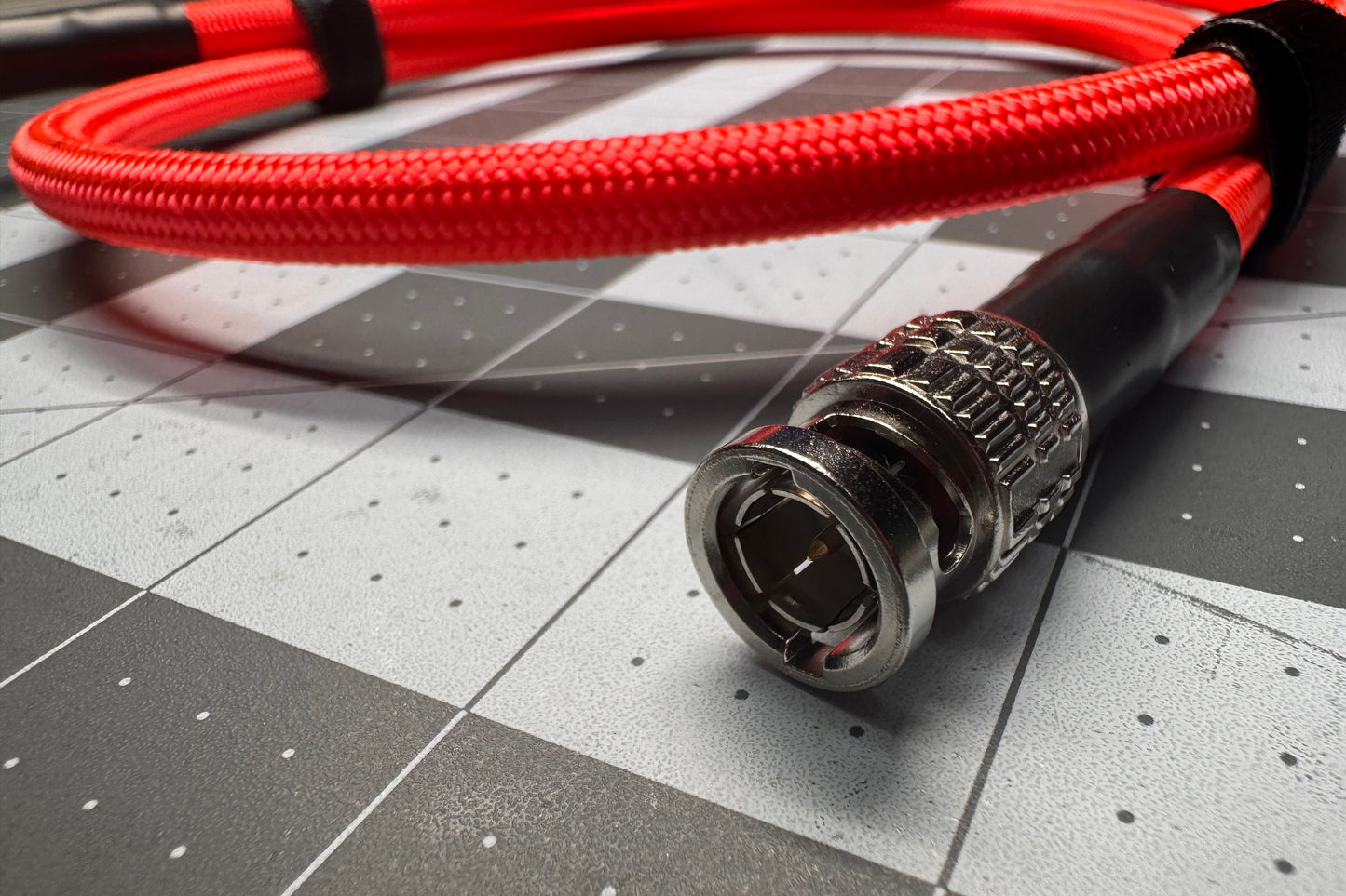 A close-up of a red braided audio cable with a silver and black BNC connector, resting on a gray and white checkered surface.