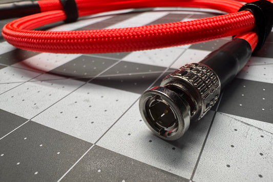 A close-up of a red braided audio cable with a silver and black BNC connector, resting on a gray and white checkered surface.