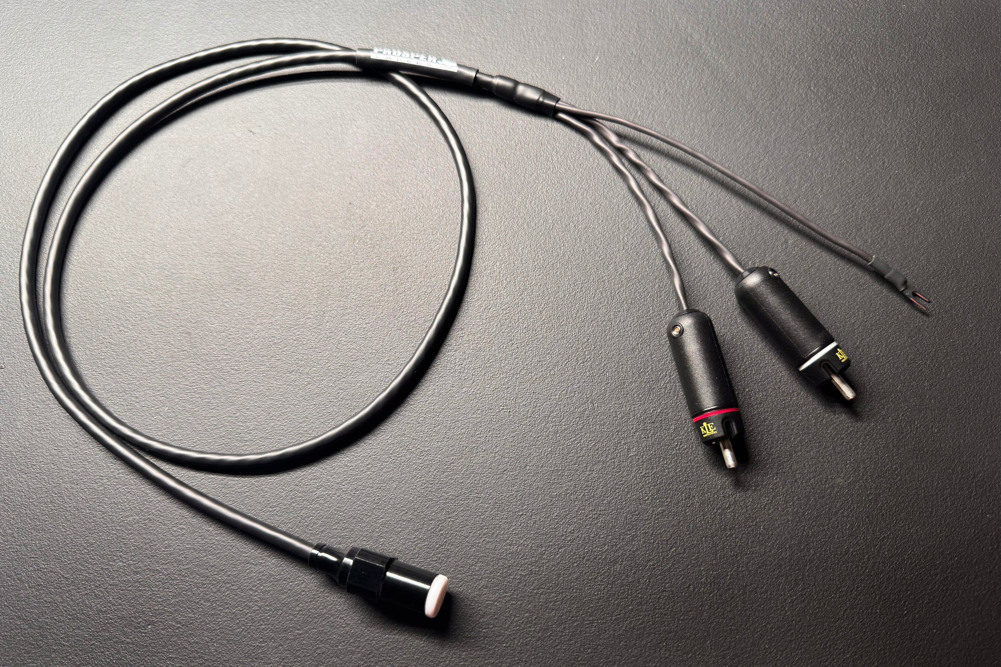 A black audio adapter cable with a 3.5mm plug on one end and two 2-pin connectors on the other, displayed on a dark textured surface.