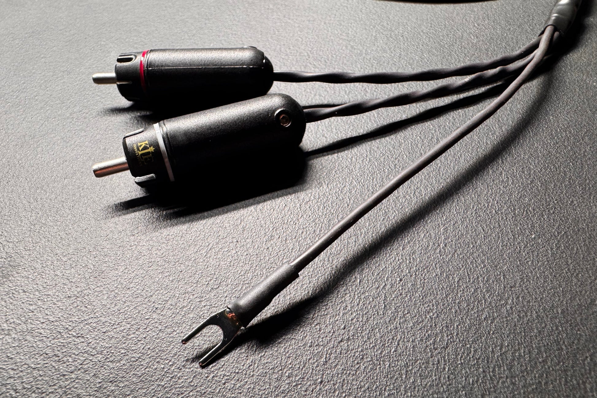 A close-up of a black audio adapter cable with two cylindrical connectors and a Y-shaped split plug, resting on a textured dark gray surface.