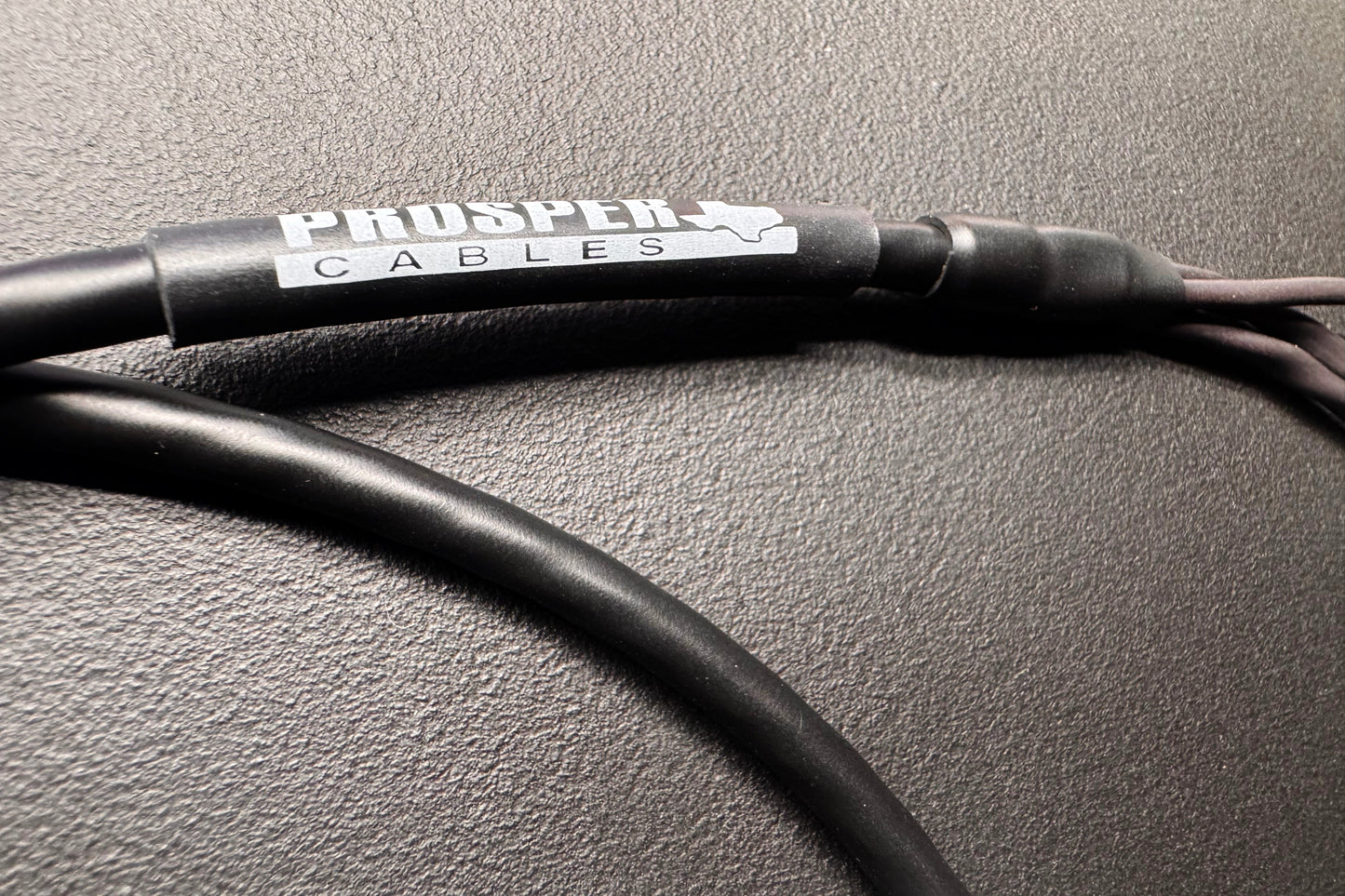A close-up of a black Prosper Cables audio cable with a silver and white brand label, resting on a textured dark gray surface.