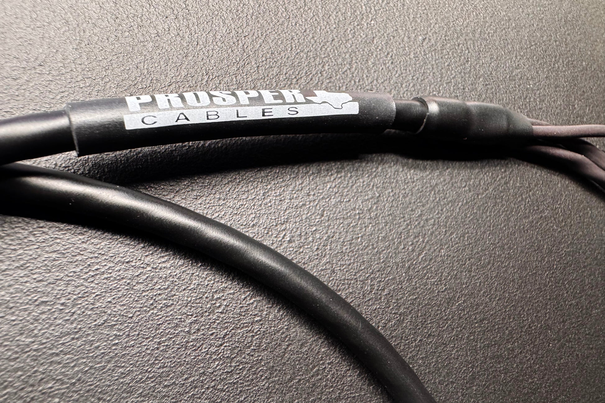 A close-up of a black Prosper Cables audio cable with a silver and white brand label, resting on a textured dark gray surface.