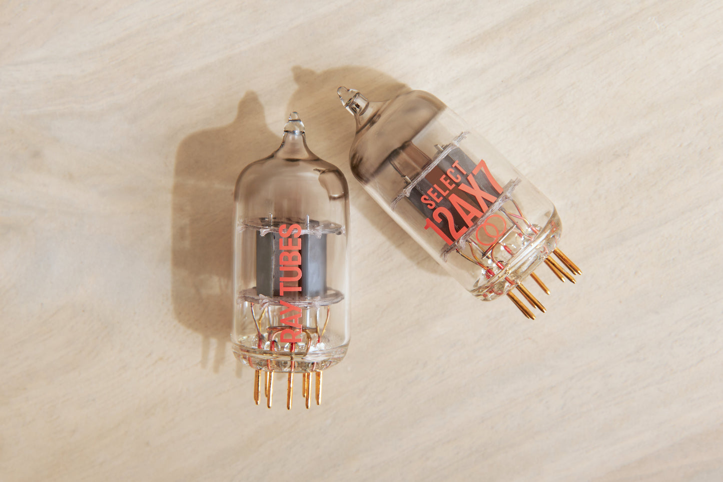 Two glass vacuum tubes, one labeled 'SELECT 12AX7' and the other 'RAY TUBES', displayed on a light wood surface.