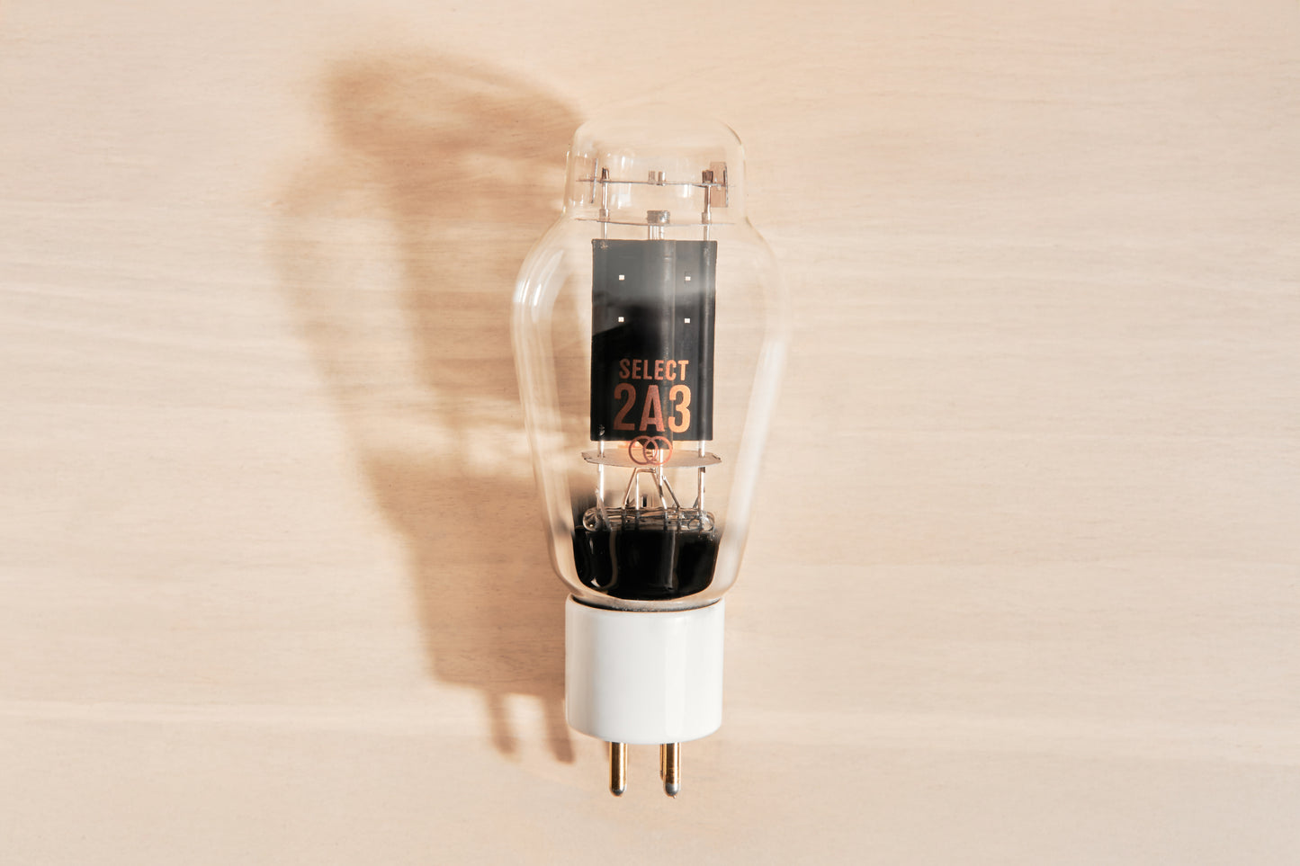 A vintage-style clear glass vacuum tube light bulb with a white base, featuring a black center label that reads 'SELECT 2A3' in orange text, set against a light wood background with a soft shadow.