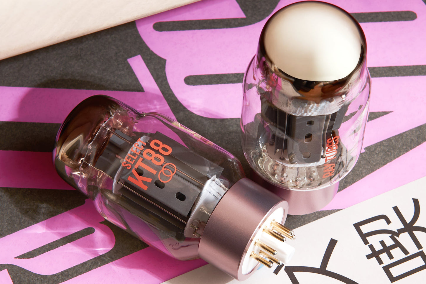 Two vacuum tubes with gold caps on a pink and black background