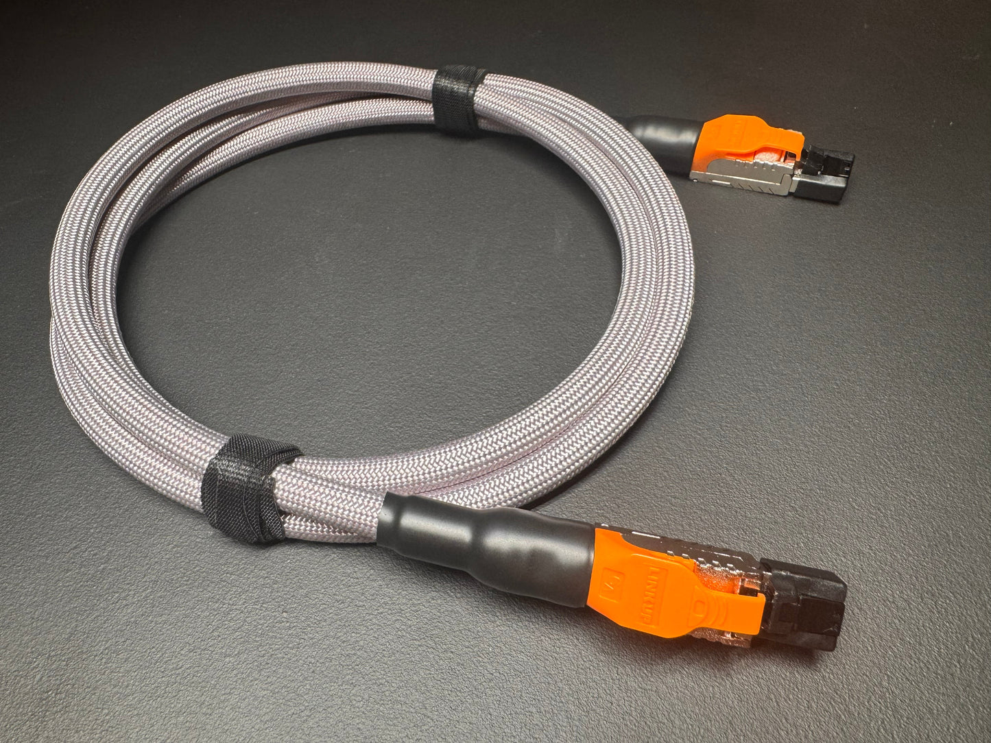 a gray and orange cable with orange connectors, lying on a gray surface.